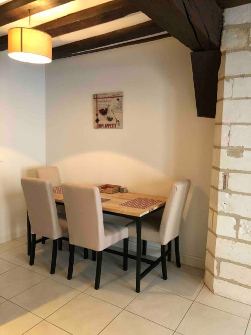 Cozy dining nook in Le Charmant Zola apartment, Troyes, with cream chairs, wooden table, exposed beams, and Bon Appetit wall