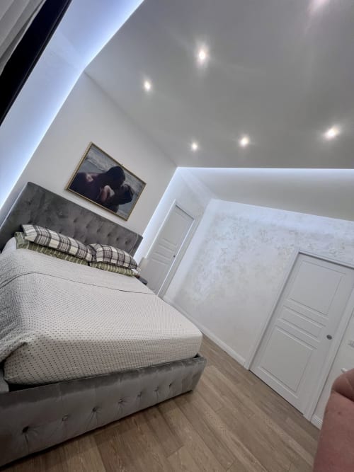 Camera da letto moderna presso Zoelia Roma con letto imbottito grigio, soffitto bianco con illuminazione incassata e pavimento in legno