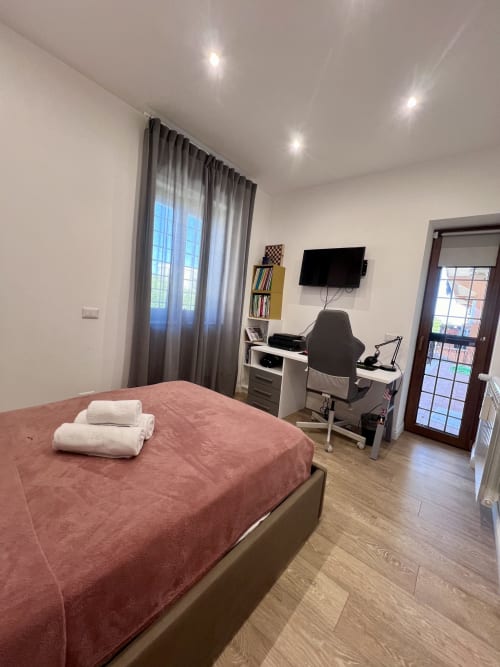 Camera da letto moderna a Zoelia Roma con letto rosa, scrivania, TV e vista sulla città dalle finestre