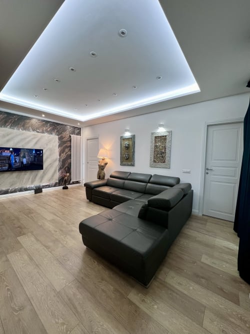 Soggiorno moderno presso Zoelia Roma con divano componibile nero, soffitto LED, parete in marmo e TV a parete