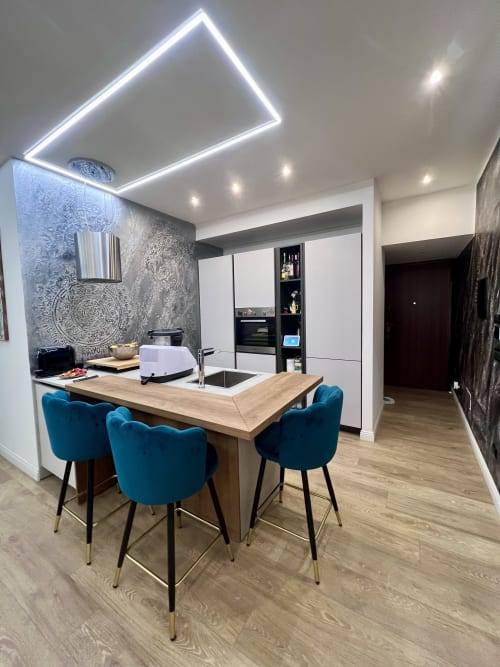 Zona cucina-pranzo moderna dell'appartamento Zoelia Roma con sedie blu, bancone in legno, mobili bianchi e soffitto neon
