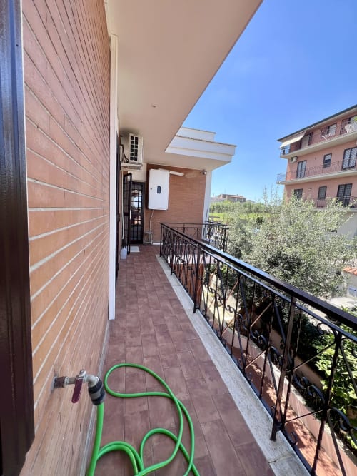 Terrazza soleggiata dell'appartamento Zoelia Roma con tubo da giardino verde, balaustra nera e vista sulla città