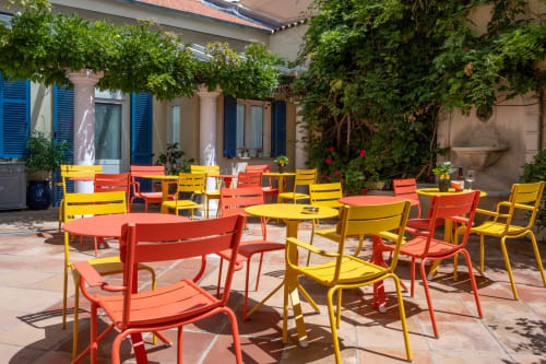 Terrazza esterna colorata dell'Hôtel De La Fontaine a Nizza con sedie rosse e gialle intorno a tavoli in stile mediterraneo