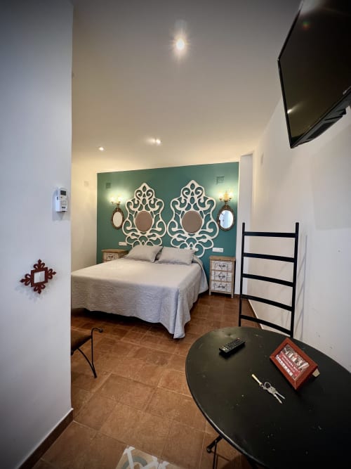 Dormitorio moderno del hotel Almagro con pared de acento verde azulado, espejos decorativos, cama blanca y mesa oscura en la sala