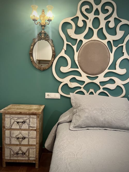 Elegant bedroom with teal walls, ornate decorative mirror, brass wall sconce, wooden nightstand, and cream bedding at Retiro