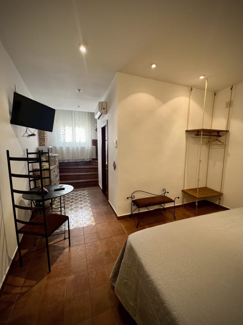 Spacious bedroom in Almagro hotel with bed, TV, desk, decorative shelving, and tiled flooring throughout