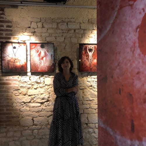 Femme en robe géométrique à la galerie Domaine de l'Ocrerie avec œuvre illuminée sur mur de briques, Pourrain