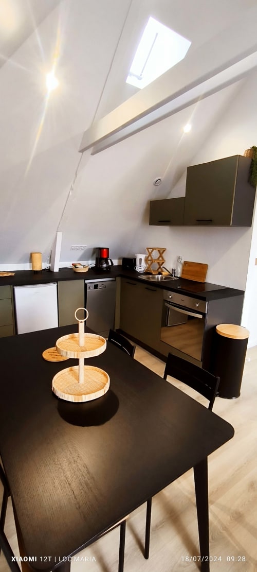 Cuisine moderne sous les toits avec mobilier noir, électroménagers inox, puits de lumière et coin repas à Belle Île en Mer