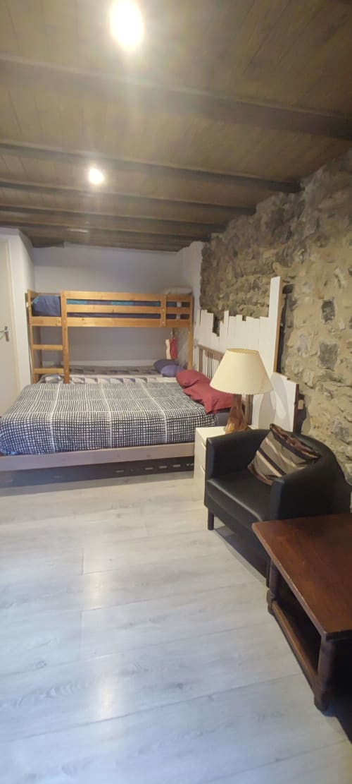 Dormitorio de albergue en La Calma De Bellver con litera de madera, sofá negro, lámpara y pared de piedra vista