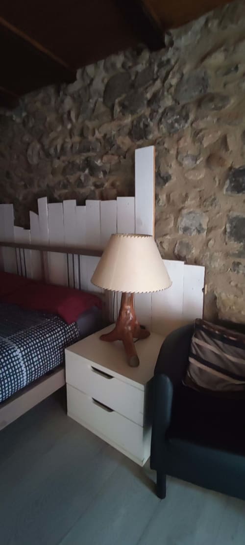 Habitación del hostal La Calma De Bellver con mesita de noche blanca, lámpara de mesa de madera y pared de piedra en Bellver de la