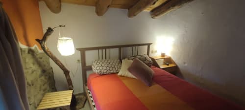 Acogedora habitación en La Calma De Bellver con ropa de cama colorida, vigas de madera y decoración rústica de ramas en Bellver de la
