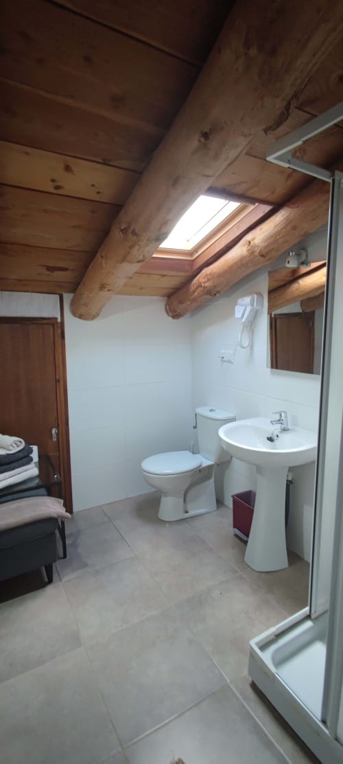 Baño espacioso en el hostal La Calma De Bellver con vigas de madera vista, claraboya, paredes blancas, inodoro y lavamanos pedestal
