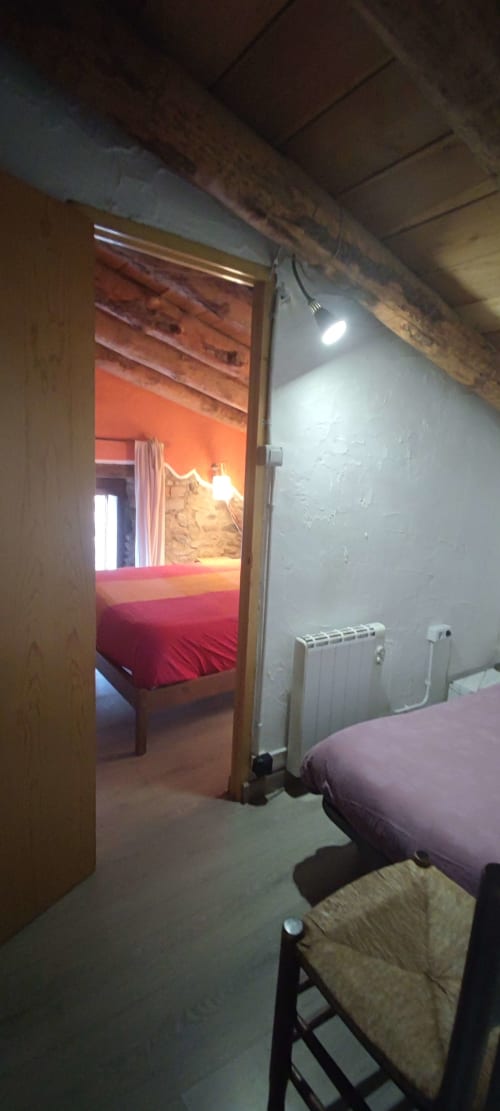 Acogedora habitación de hostal en La Calma De Bellver con cama roja, paredes blancas, vigas vistas y radiador de calefacción