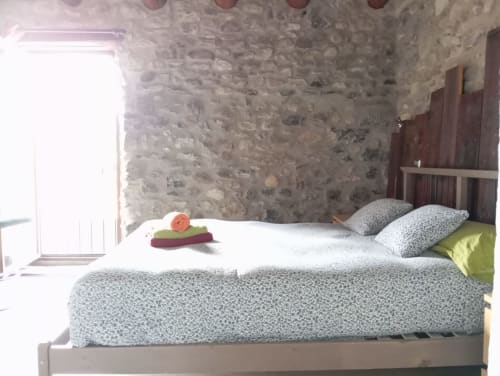 Habitación luminosa en el hostal La Calma De Bellver con muros de piedra, camas gemelas, ropa de cama gris y luz natural de la ventana