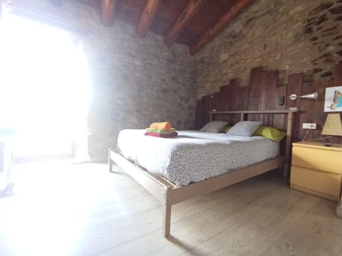 Habitación luminosa en el hostal La Calma De Bellver con cama de madera, paredes de piedra, techo de vigas y vistas a la montaña