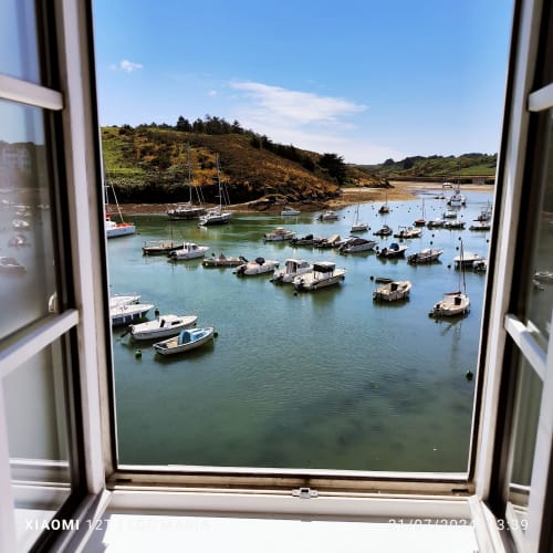 Fenêtre ouverte sur le port avec bateaux amarrés et versant verdoyant à Locmaria, Belle Île en Mer