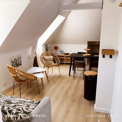 Appartement mansardé moderne à Belle Île-en-Mer avec chaises en rotin, table à manger et baies vitrées offrant vue sur mer