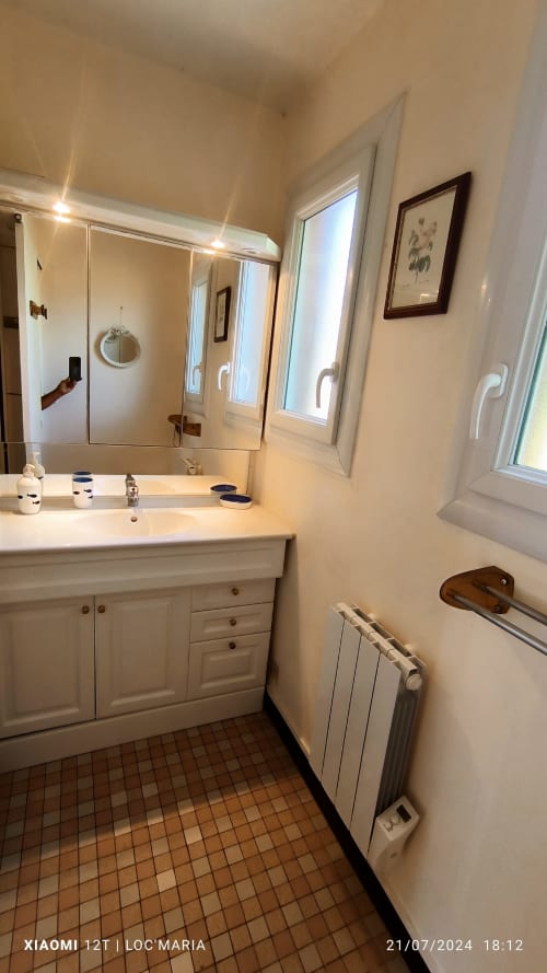 Salle de bains moderne du gîte Loc'Maria avec vasque blanche, miroir, radiateur et carrelage en terre cuite, Belle-Île-en-Mer