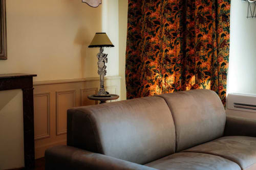 Chambre élégante à Mes à Moi Pézenas avec canapé en cuir gris, lampadaire orné et rideaux à motifs orange vif