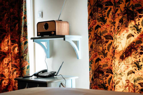 Télévision vintage et téléphone à cadran sur étagères blanches à la maison d'hôtes Mes à Moi Pézenas, encadrés par des rideaux floraux orange ornementés