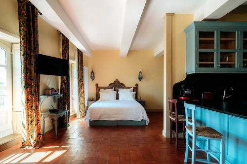 Chambre spacieuse à Mes à Moi Pézenas aux murs jaunes, lit en bois, kitchenette et carrelage terra cotta