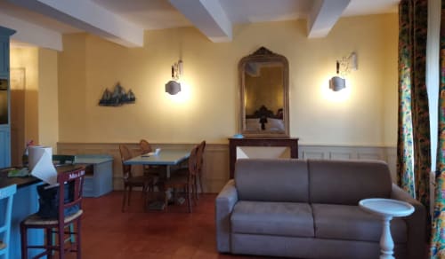 Lounge aux murs jaune éclatant chez Mes à Moi Pézenas avec canapé gris, table à manger et miroir décoratif