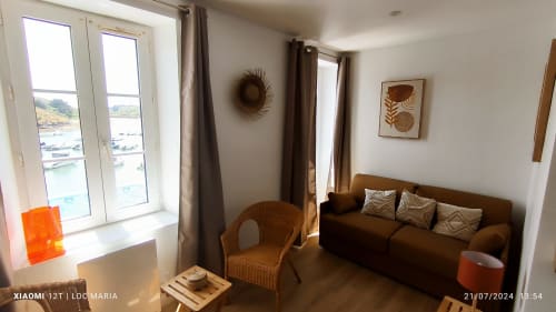 Studio lumineux avec vue mer, canapé marron, fauteuil en rotin et décoration côtière à Loc'Maria Belle Île en Mer