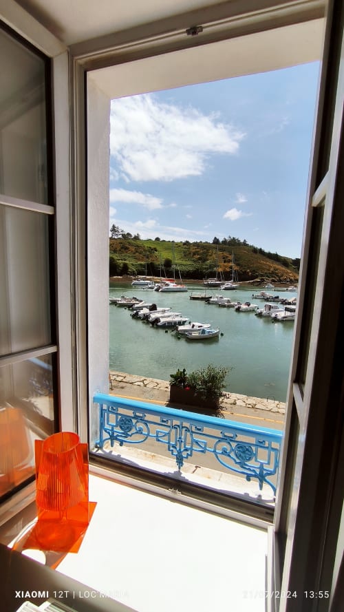 Vue depuis la porte ouverte du port turquoise avec bateaux amarrés, flanc de colline et balustrade bleue à Studio La Reine de Guerveur, Belle Île en