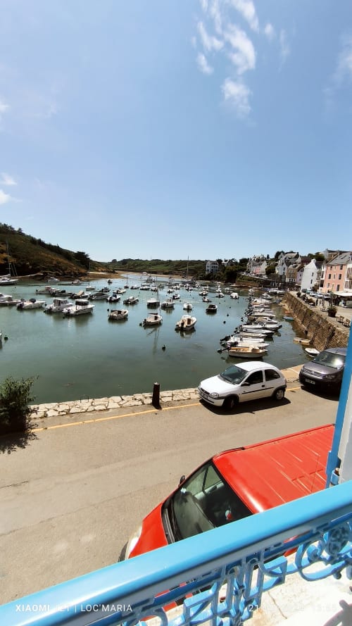 Port de pêche coloré à Locmaria, Belle Île avec bateaux amarrés, voitures garées et bâtiments côtiers en pierre sous un ciel bleu
