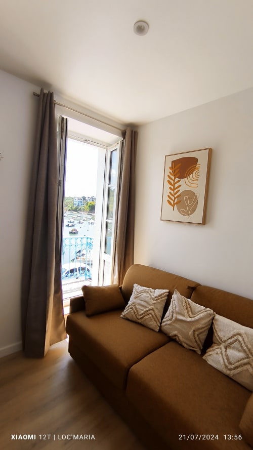 Studio avec canapé marron, vue mer par les portes-fenêtres ouvertes, art abstrait moderne sur murs crème à Loc'Maria, Belle