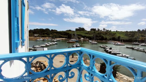 Balustrade bleue donnant sur les voiliers amarrés du port de Locmaria, Belle Île en Mer, avec colline verdoyante en arrière-plan
