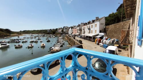 Balustrade bleue surplombant le port de Locmaria avec bateaux amarrés, bâtiments du village côtier et restaurants en bord de mer à Belle