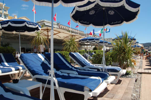 Zona lounge sulla spiaggia dell'Hôtel De La Fontaine a Nizza con lettini blu, ombrelloni neri e vista sul Mediterraneo
