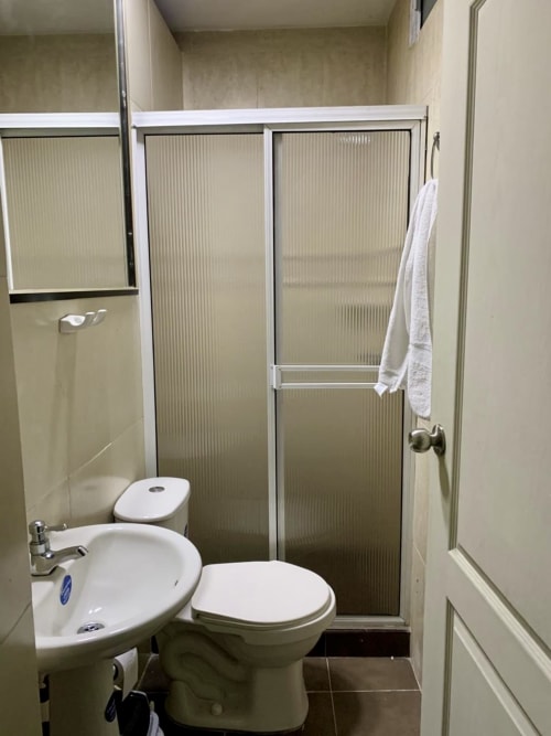 Baño compacto del hotel Casa Mango en Cali con inodoro, lavamanos y cabina de ducha con puertas de vidrio texturizado