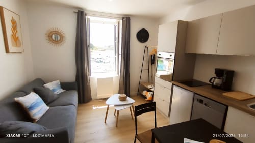 Studio avec vue mer, canapé gris, cuisine blanche et fenêtre sur Locmaria, Belle-Île-en-Mer