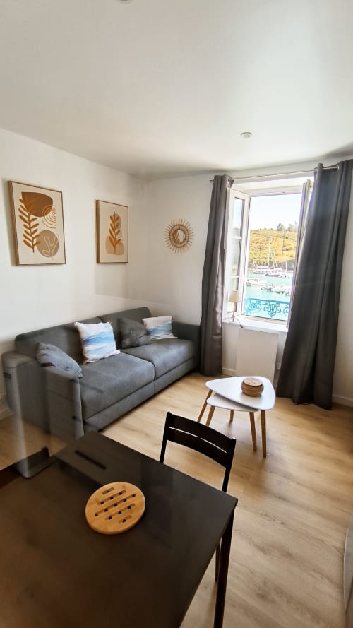 Studio moderne à Locmaria, Belle Île avec vue mer, canapé gris, table basse blanche et décoration murale thème nautique
