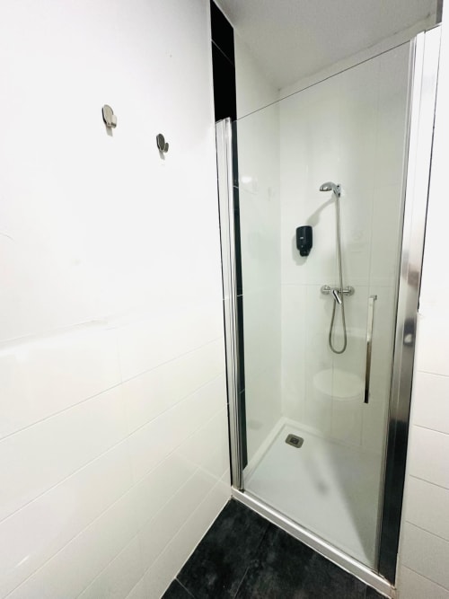 Moderno baño de apartamento Gestyp-AT en Mérida con ducha de cristal, paredes de azulejos blancos y piso oscuro