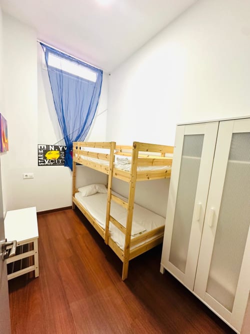 Acogedora habitación con litera de madera, ropa de cama blanca, cortinas azules y piso de madera en Mérida.