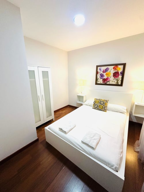 Dormitorio moderno en apartamento Gestyp-AT en Mérida con cama blanca, obras florales, pisos de madera y vista al jardín