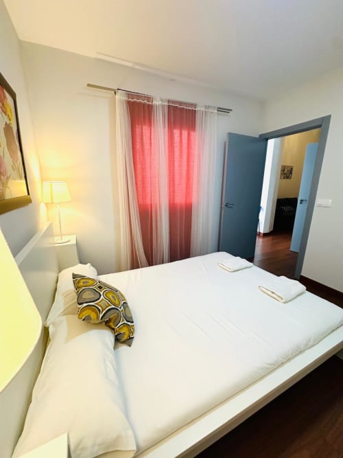Moderno dormitorio en apartamento Gestyp-AT Mérida con cama blanca, cortinas rojas y vistas al jardín