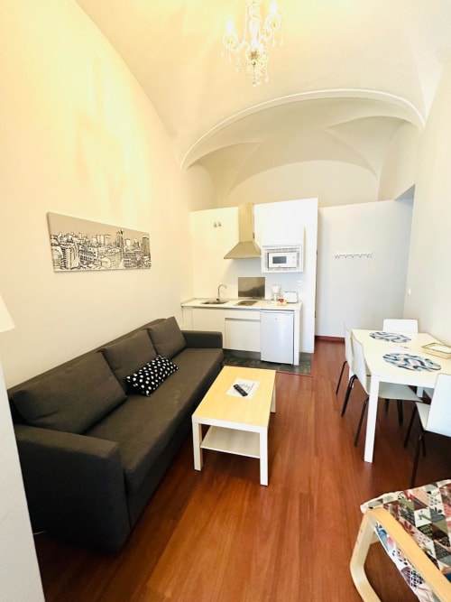 Sala moderna en Mérida con sofá negro, kitchenette, mesa de comedor blanca y elegante detalle de techo curvo