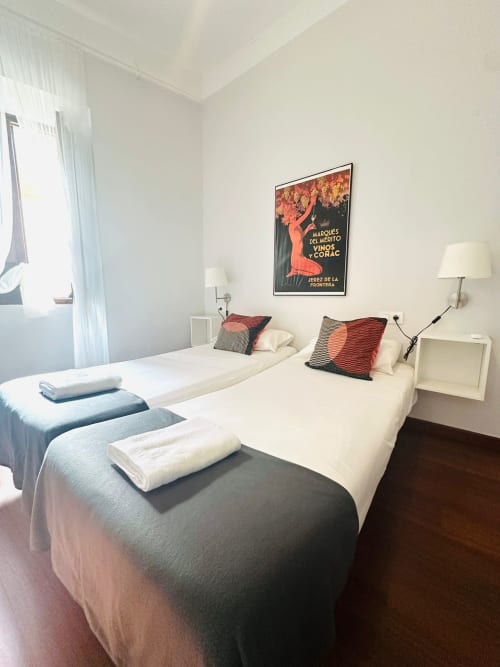 Dormitorio luminoso en apartamento Gestyp-AT de Mérida con camas gemelas, póster vintage de vino español y muebles modernos.