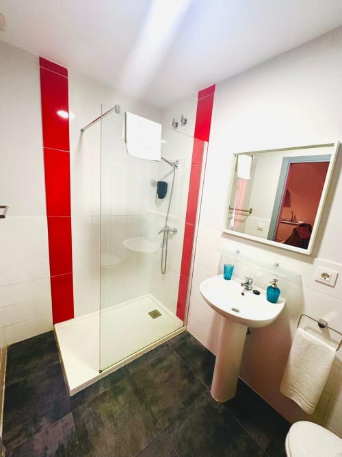 Baño moderno con azulejos rojos, ducha a ras de piso, lavamanos de pedestal y espejo en apartamento Gestyp-AT, Mérida