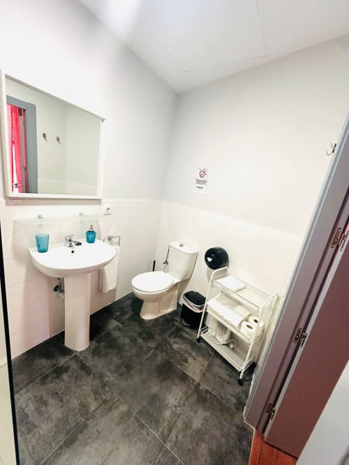 Baño moderno y limpio en apartamento Gestyp-AT, Mérida, con lavabo blanco, inodoro, espejo y piso de azulejos grises.