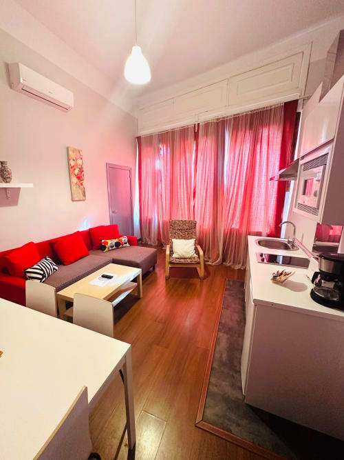 Luminoso departamento en Mérida con sofá rojo, cocina moderna y cortinas rosadas con vista al monumento