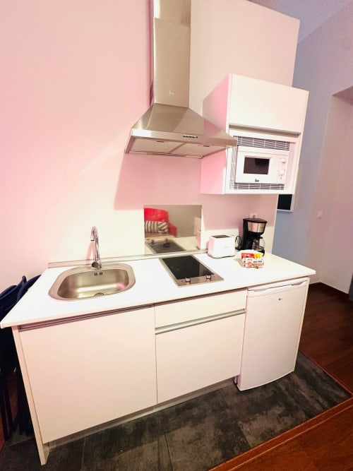 Cocina compacta rosa y blanca en apartamento de Mérida con estufa, fregadero, microondas y armarios altos