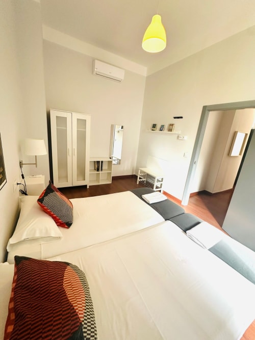 Moderno dormitorio de apartamento en Mérida con camas gemelas, muebles blancos, lámpara colgante amarilla y pisos de madera