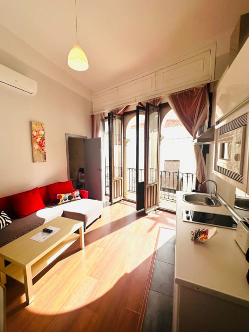 Apartamento luminoso en Mérida con sofá rojo, cocina y balcón con vistas a los monumentos