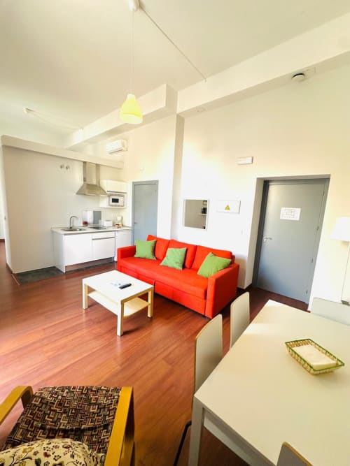 Sala moderna con sofá rojo, cocina abierta y pisos de madera en Gestyp-AT, Mérida
