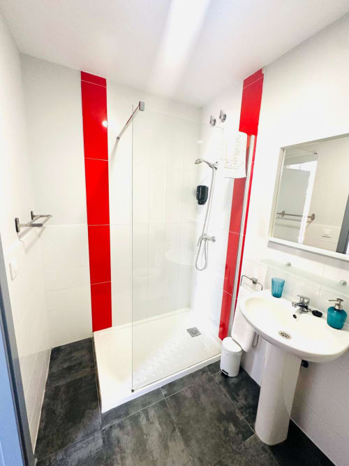 Baño moderno en apartamento Gestyp-AT, Mérida con azulejos rojos de acentuación, ducha abierta, lavamanos pedestal y piso de azulejos oscuros